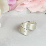 Personalised adjustable silver ring. The ring band is 7mm wide and wraps around the finger like a ribbon. The personalisation can be added on the outside or the inside of the ring. Space is limited but you can add symbols or letters of your choice. This ring has two stars at either end and a matte finish.