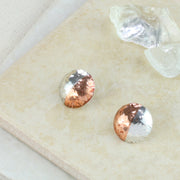 Round stud earrings with one half in copper and the other half in silver. They have been domed with the curve facing outwards. They're available with a stiped texture or a round texture and have a shiny mirror finish.