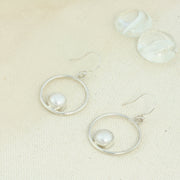 Silver hoop hook earrings featuring a freshwater pearl. The  pearl is 8mm in diameter and is set in a cabochon setting at the bottom on the inside of the hoop. These are handmade earrings, made form eco-silver.