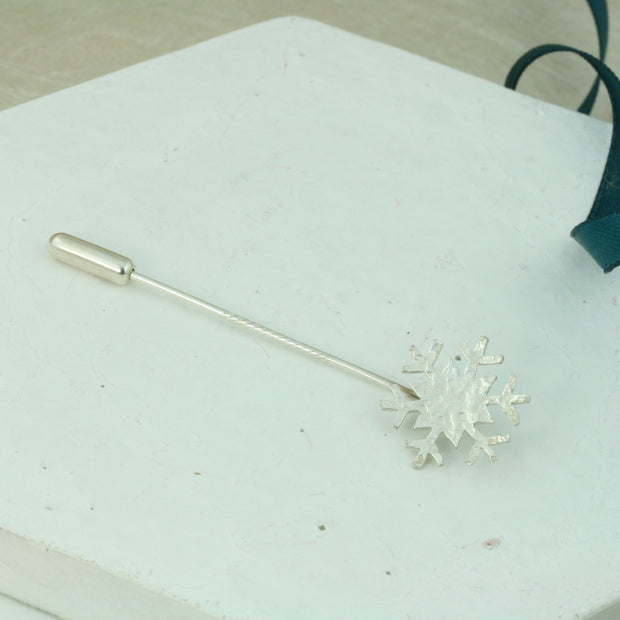 Silver pin featuring a six sided snowflake. The snowflake has a hammered and shiny finish which captures the light to make it sparkle. The pin can be worn as a hat pin, or brooch on a scarf or jacket.