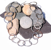 Silver statement necklace featuring silver hoops in various sizes and various hammered textures. Two hoops near the middle of the necklace are made from copper and have a hammered texture as well. The necklace has a shiny finish.