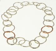 Silver statement necklace featuring silver hoops in various sizes and various hammered textures. Two hoops near the middle of the necklace are made from copper and have a hammered texture as well. The necklace has a shiny finish.