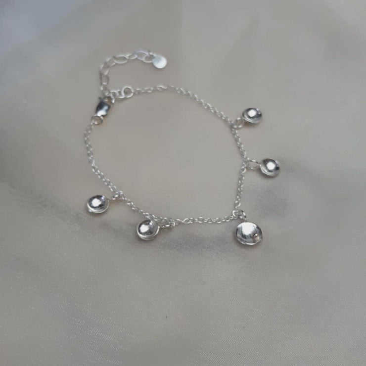 Silver bracelet with 5 domed cups attached to the chain a charms. The middle cup is slightly bigger than the others and features a gold ball. The cups have a slightly striped or pebble texture and mirror finish.