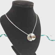 Silver pendant necklace featuring a circle that has been cut in half. Both sides have been domed into half a cup shape and soldered together with the dome on different sides. One side has a striped texture the other a round hammered texture. It has an oxidised darker finish. The snake chain necklace is 40 cm / 15" long.