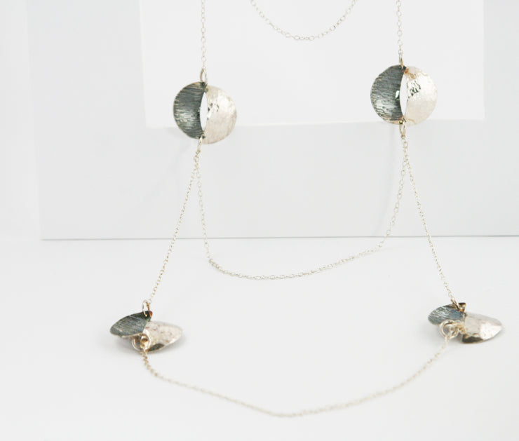 Silver statement necklace with 3 split circles on either side, connectes vertically and horizontally by chain. The  circles are split in half and domed, then soldered together in opposite directions. Both sides have a different hammered texture , one half has a shiny mirror finish, the other an oxidised buffed finish.