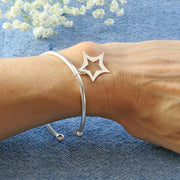 Eco silver bangle bracelet made form round wire 3mm / 0.1" in diameter. With a silver ball on both ends, featuring a star charm of about 20mm / 0.8" in diameter with curved sides and a star opening in the centre.. One side has a hammered texture with a shiny finish, the other a mirror finish.