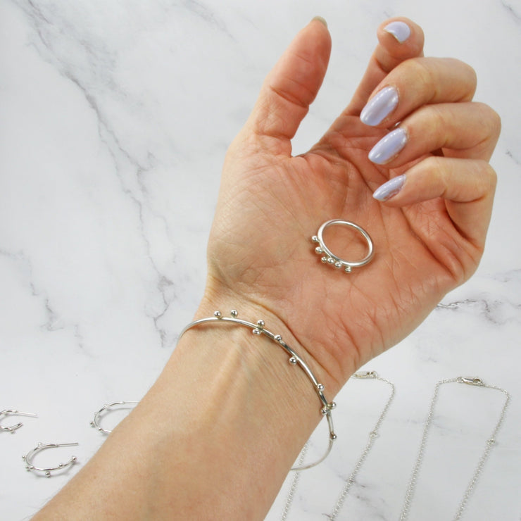 Eco silver bangle with ten silver balls on a model. Also showing the eco silver ring with silver balls and and matching earrings and necklace on a marble background.