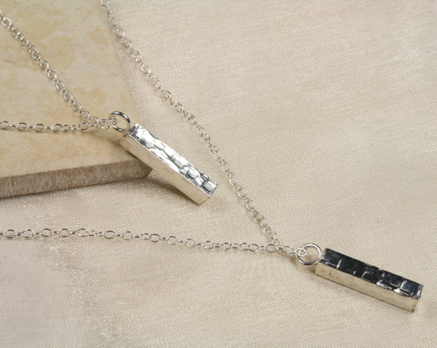 Eco silver pendant necklace featuring two bars. Both have a square hammered texture and shiny mirror finish. They are attached to two chain with different lengths letting one bar sitting above the other.