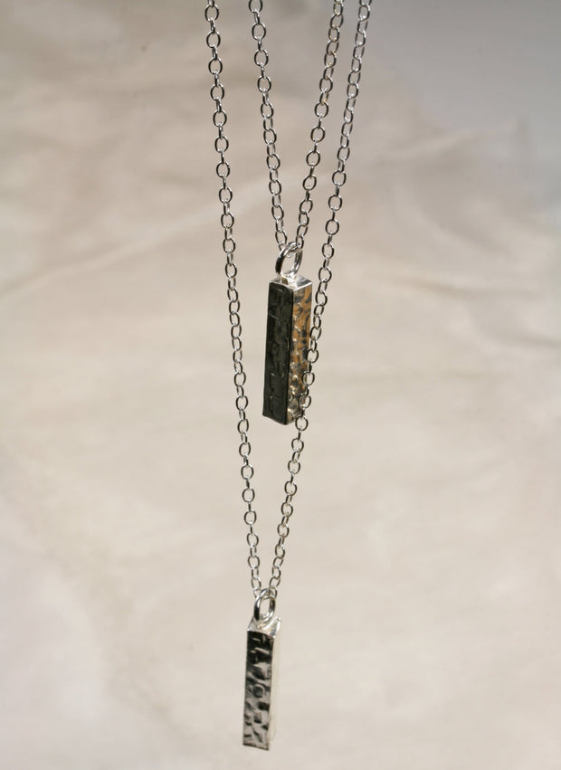 Eco silver pendant necklace featuring two bars. Both have a square hammered texture and shiny mirror finish. They are attached to two chain with different lengths letting one bar sitting above the other.