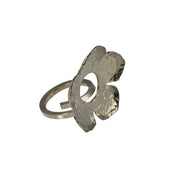 Large silver flower with its centre cut out. The flowr has a hammered texture and shiny finish and sits on a squre ring band tht is kept open so the ring is adjustable in size.