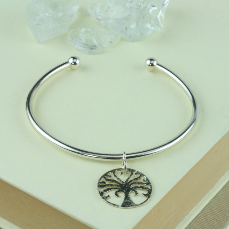 Silver bangle with a silver Tree of Life charm. A silver ball on each end of the bangle keeps the charm in place. The charm has a textured finish on one side and a mirror finish on the other.
