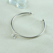 Eco silver bangle with a small rainbow charm. It is attached to the bangle with a jump ring, so it moves freely around the bangle. The bangle has a silver ball on each end and can be adjusted in width by pulling or pinching it gently. The rainbow features three arches made from round eco silver wire. The whole piece has a shiny mirror finish.