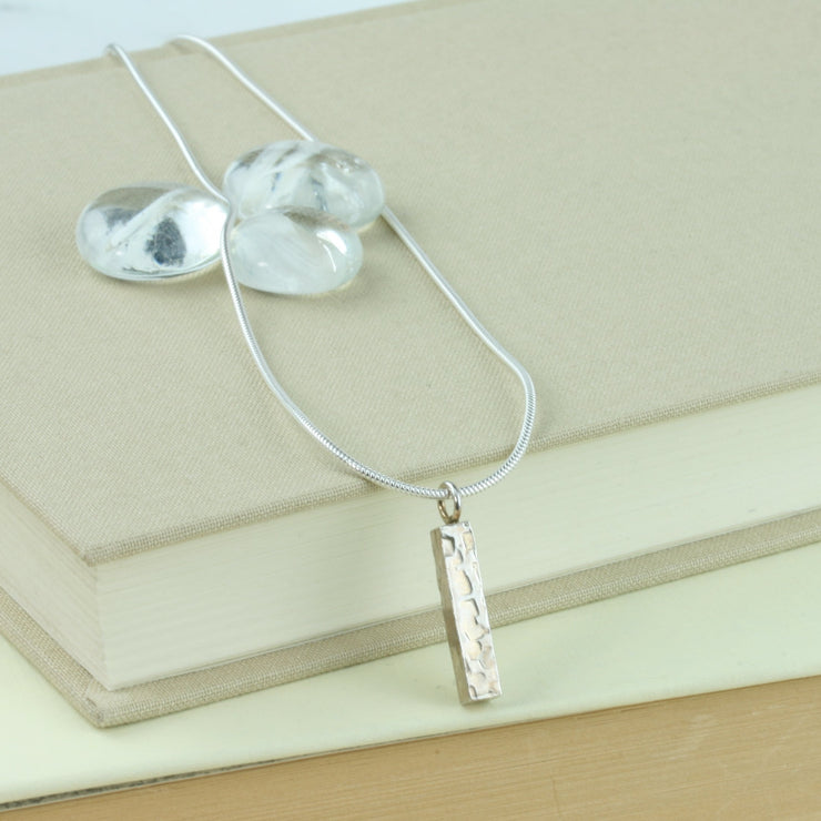Eco silver bar with a square hammered texture. It has shiny mirror finish and dangles from a snake chain.