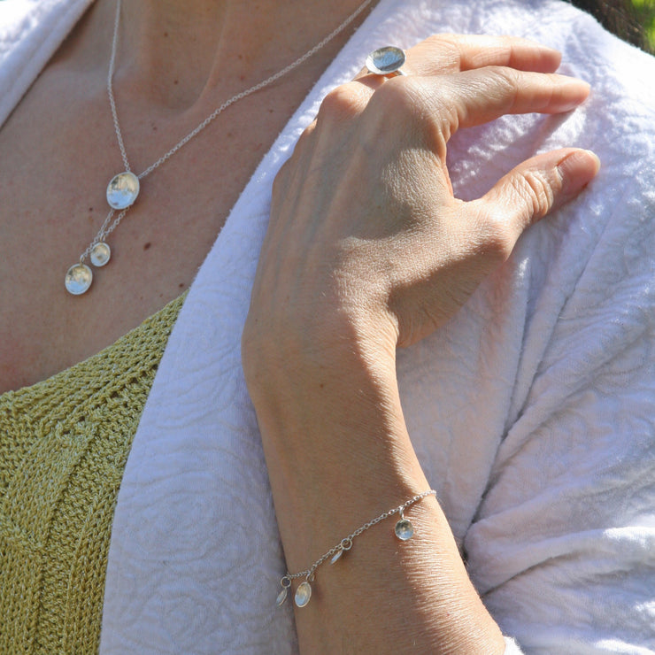 Silver bracelet featuring five domed cups. The middle cups is slightly larger than the other 4. It is fastened with a lobster clasp and can be fastened at different lengths. The cups have a stripe texture.