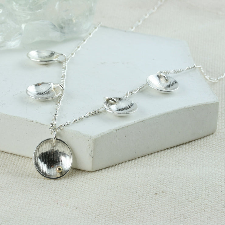 Silver necklace with 5 domed cups. There are 4 smaller cups and one larger cup which features a 9ct gold ball. The cups have a stripe texture and a mirror finish.