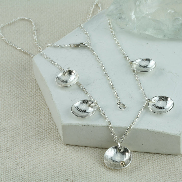 Silver necklace with 5 domed cups. There are 4 smaller cups and one larger cup which features a 9ct gold ball. The cups have a stripe texture and a mirror finish.