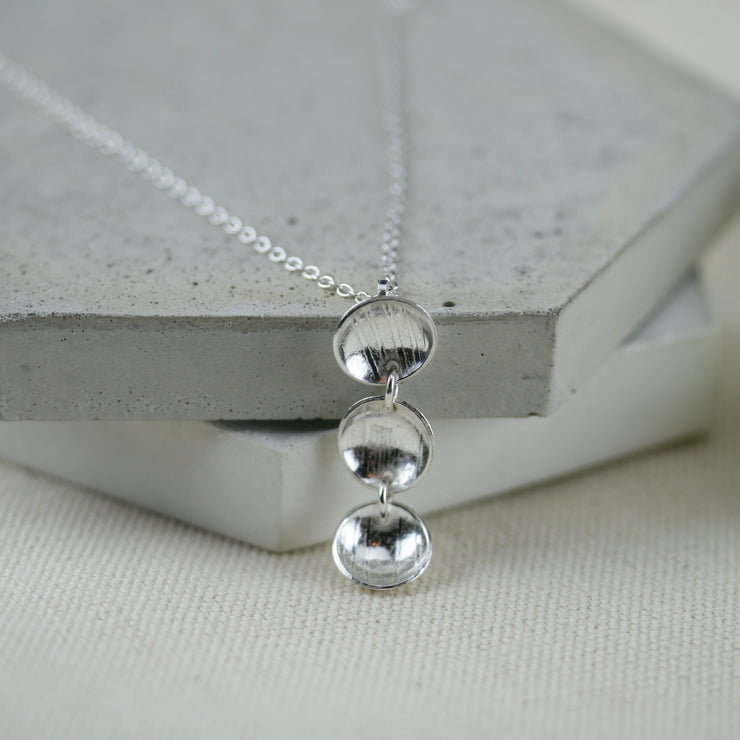 Silver sups pendant necklace featuring three silver domed cups attached to each other by jump rings to form a vertical pendant. The three cups feature a pebble or stripe texture and have a mirror finish.
