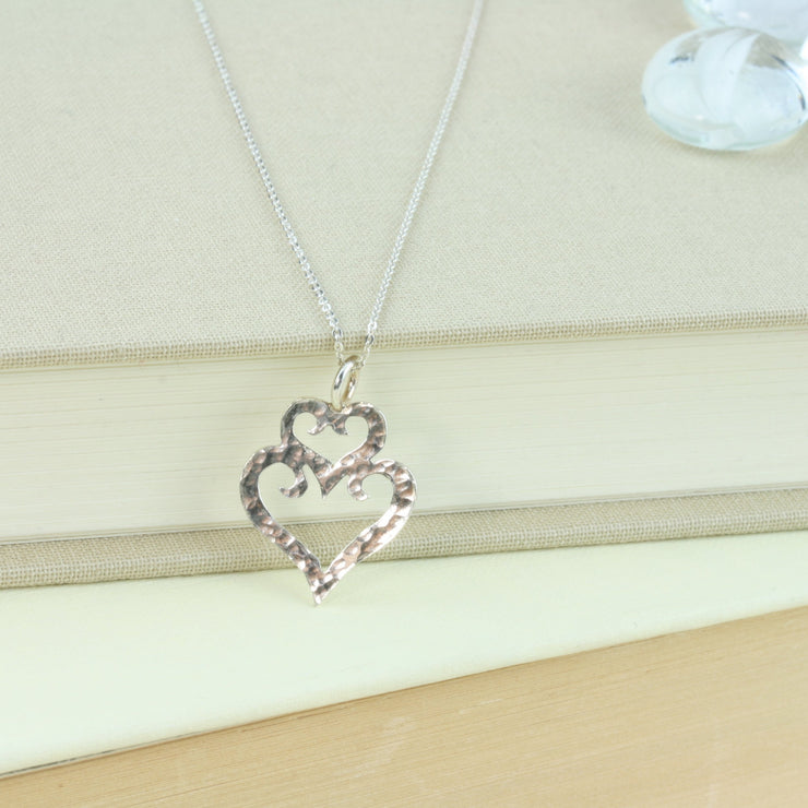 Eco silver pendant necklace with a double heart shape. The smaller heart sits on top of the larger heart as a small crown. With a hammered silver finish.
