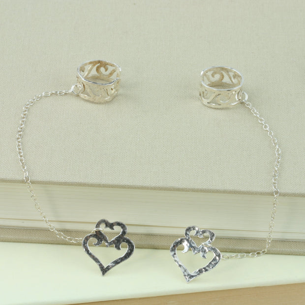 Eco silver hearts stud earrings with half heart ear cuffs. Both are attached to each other with silver chain. The ear cuffs feature 5 half hearts, that sit like swirls in a silver band.
