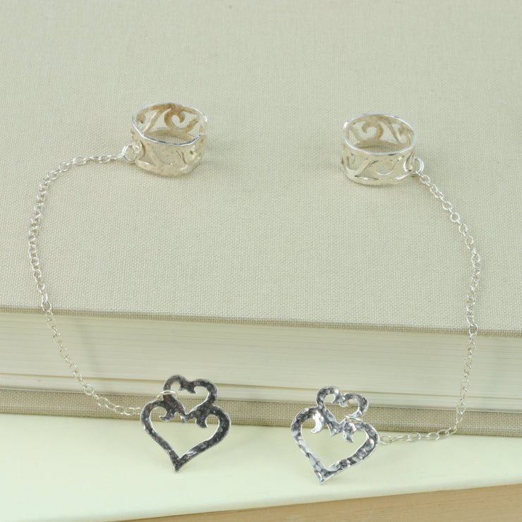Eco silver hearts stud earrings with half heart ear cuffs. Both are attached to each other with silver chain. The ear cuffs feature 5 half hearts, that sit like swirls in a silver band.
