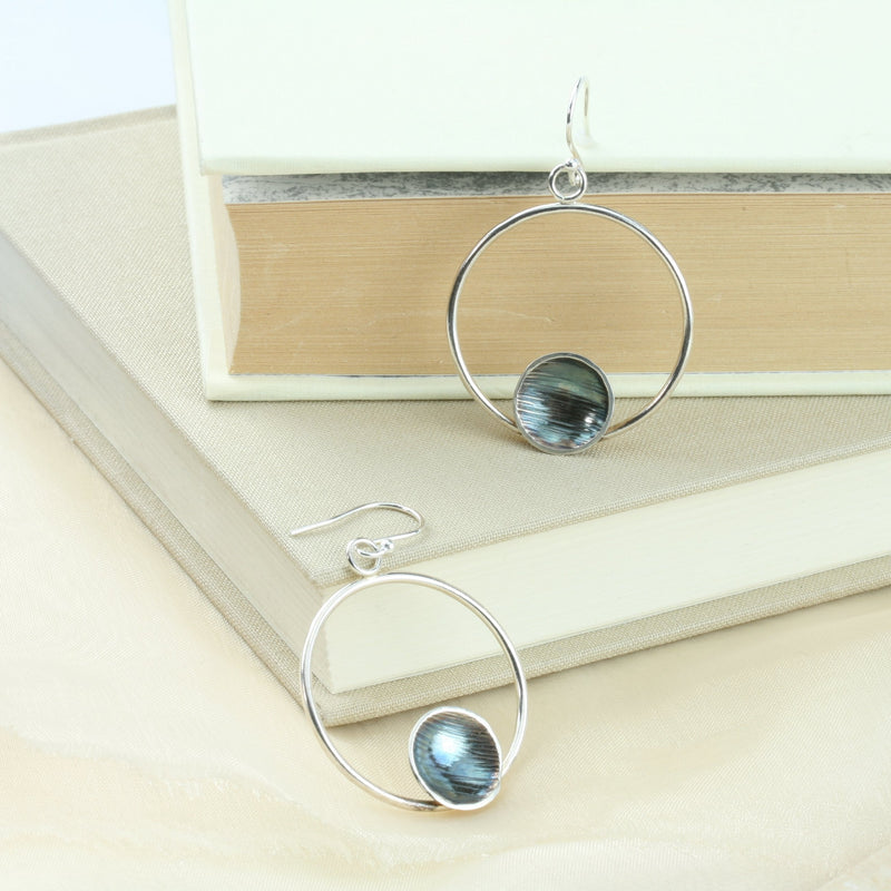 Eco silver hoop earrings with a dish on the inside at the bottom of the hoop. The hoop it attached to a hook earrings at the top. The hoops have a shiny miror finish and the cups have a striped texture with a darker oxidised finish. The cups are polished to a shine as well. The backs of the cups have a mirror finish.