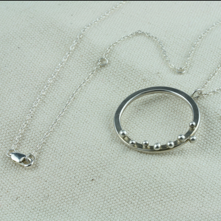 Eco silver hoop pendant necklace. The hoop is flat and has 8 silver balls. The trace chain necklace can be fastened at three different lengths with the lobster clasp.