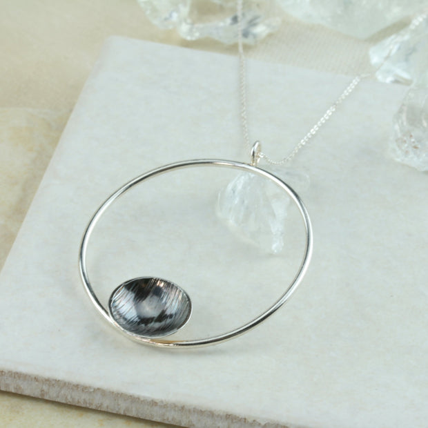 Eco silver hoop pendant necklace with dish. The hoop has a shiny mirror finish and features a silver domed dish on the inside bottom. The dish has a hammered texture and the inside is oxidised and polished to show a darker finish in contrast to the hoop.