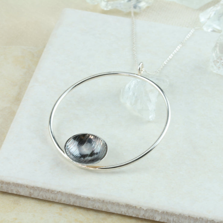 Eco silver hoop pendant necklace with dish. The hoop has a shiny mirror finish and features a silver domed dish on the inside bottom. The dish has a hammered texture and the inside is oxidised and polished to show a darker finish in contrast to the hoop.