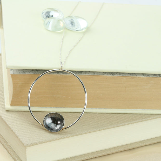 Eco silver hoop pendant necklace with dish. The hoop has a shiny mirror finish and features a silver domed dish on the inside bottom. The dish has a hammered texture and the inside is oxidised and polished to show a darker finish in contrast to the hoop.