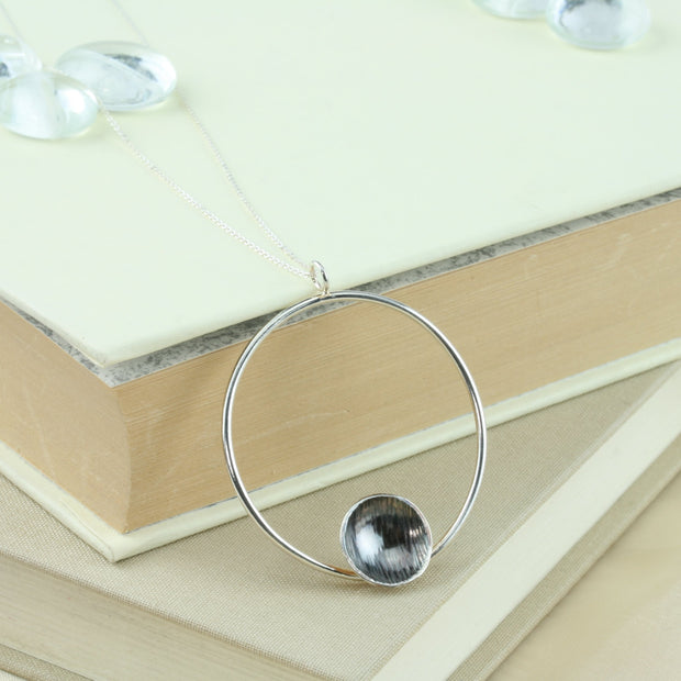 Eco silver hoop pendant necklace with dish. The hoop has a shiny mirror finish and features a silver domed dish on the inside bottom. The dish has a hammered texture and the inside is oxidised and polished to show a darker finish in contrast to the hoop.