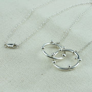 Silver necklace featuring two hoops, one larger and one smaller hoop. With 5 silver balls on the smaller hoop and 6 silver balls on the larger hoop. The silver trace chain is attached to both hoops and fastens with a lobster clasp. The necklace is 45 cm / 18" long.