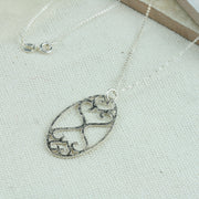 Oval shaped pendant necklace featuring a smaller heart and a larger heart at the top and the same shapes mirrored at the bottom. The pendant is sawn by hand and has been given a hammered shiny finish.