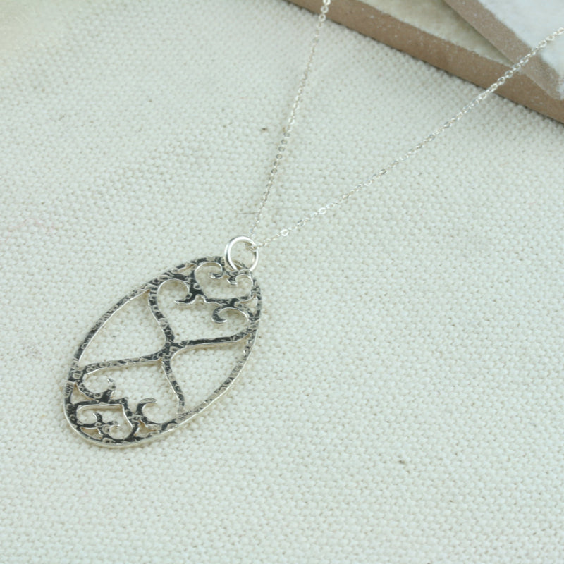 Oval shaped pendant necklace featuring a smaller heart and a larger heart at the top and the same shapes mirrored at the bottom. The pendant is sawn by hand and has been given a hammered shiny finish.