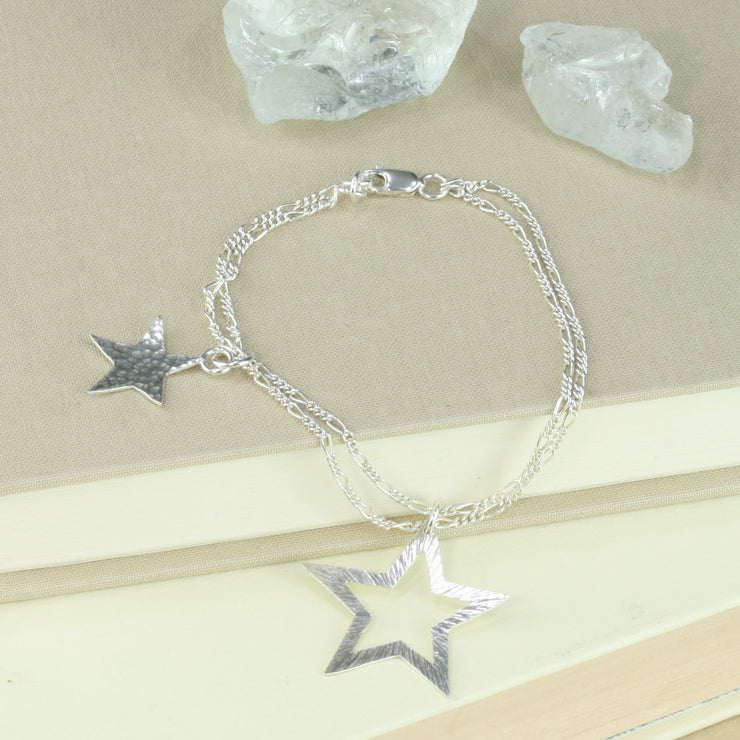 Silver bracelet featuring two stars made from eco silver. They both have a mirror finish at the back and a hammered finish at the front. The larger star has a striped texture and smaller star that has been sawn out of the larger star has a round texture at the front. The two figaro chains are the perfect finish to this shiny bracelet.