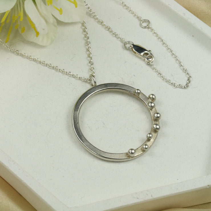 Eco silver hoop pendant necklace. The hoop is flat and has 8 silver balls. The trace chain necklace can be fastened at three different lengths with the lobster clasp.