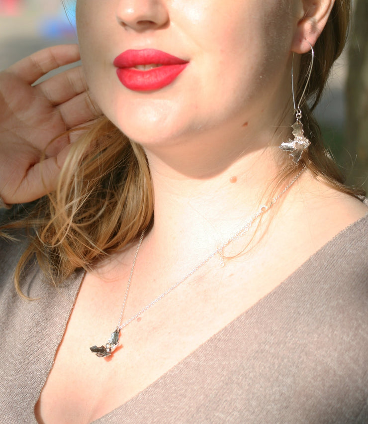 Eco silver long wired earring hooks with holly dangling from the bottom. The holly has a hammered texture and aged darker finish which has been polished to a shine. In the centre three berries are featured. They have a shiny silver finish which contrasts with the darker leaves. Seen here with the matching silver holly pendant necklace. 