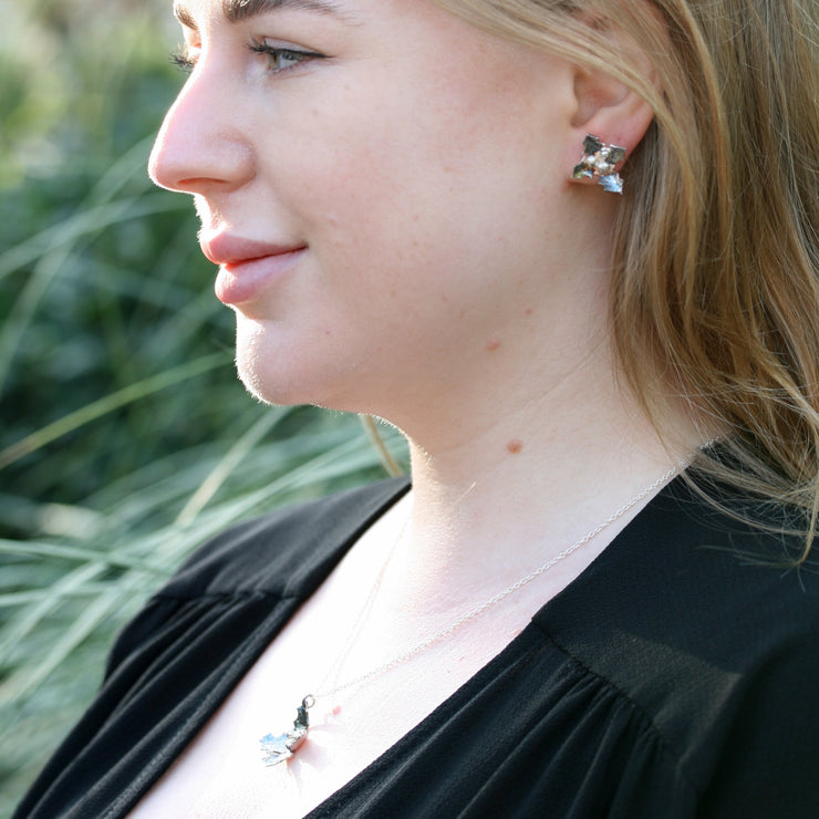 Silver holly stud earrings. Earrings in the shape of holly with four leaves and three berries in the centre. The leaves have been oxidised to give them a darker finish. They also feature a hammered texture so they sparkle and shine. Seen here with the matching pendant necklace.