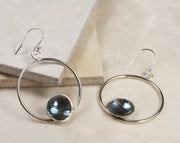 Eco silver hoop earrings with a dish on the inside at the bottom of the hoop. The hoop it attached to a hook earrings at the top. The hoops have a shiny miror finish and the cups have a striped texture with a darker oxidised finish. The cups are polished to a shine as well. The backs of the cups have a mirror finish.