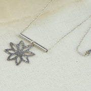 Silver pendant necklace with a flower shape with pointed sharp petals dangling off a round branch. The pendant and necklace have a shiny finish.