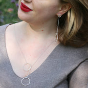 Silver earrings featuring a small hoop at the top with a stud attached to go through the ear. Chain is attached to the small hoop with a jump ring. At the bottom a larger hoop is featured. The hoops have a hammered texture and a sparky shiny finish. A matching y necklace is available, as shown in this photo.