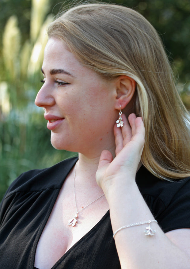 Silver hook earrings featuring Mistletoe with a silver ball as a berry. The leaves have a striped texture and a shiny silver finish. The total drop is 2.5cm from the hook. Shown here in combination with the matching pendant necklace and bracelet.