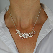 Silver necklace featuring a pendant with 6 different sized swirls. They all have a striped texture all completed with a snake chain to feature them.