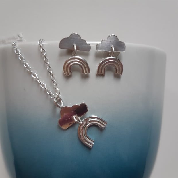 Set of eco silver earrings and pendant necklace featuring a cloud shape with a rainbow underneath. The rainbow is attached to the cloud by a jump ring and dangles down.