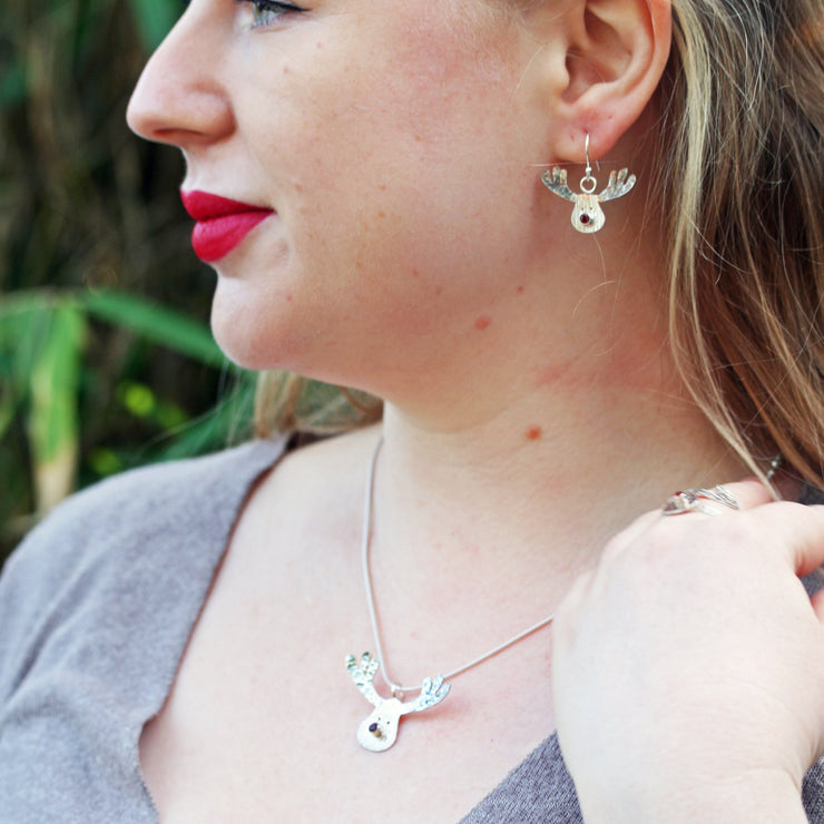 Silver hook earrings featuring a sawn out Rudolph head. The face has a striped texture and shiny silver finish. The Antlers have a round hammered texture and are aged to give them a darker look, they have been polished to a shine. The red nose is a Garnet gemstone set in a tube setting. A matching pendant necklace and ring are available as well. 