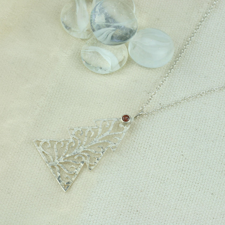 Silver pendant necklace in the shape of a Christmas three with three layers. The tree features a hand drawn pattern which is hand sawn with swirls from the centre to the sides. It has a hammered texture which has been polished to a shiny finish, giving it a shimmer effect. Seen here with a matching set of silver Christmas tree hook earrings.