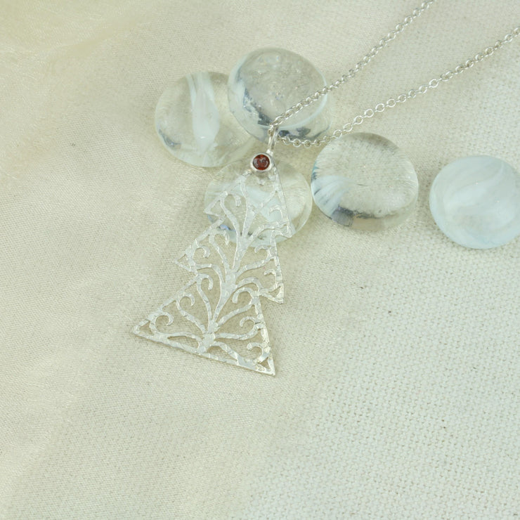 Silver pendant necklace in the shape of a Christmas three with three layers. The tree features a hand drawn pattern which is hand sawn with swirls from the centre to the sides. It has a hammered texture which has been polished to a shiny finish, giving it a shimmer effect. Seen here with a matching set of silver Christmas tree hook earrings.