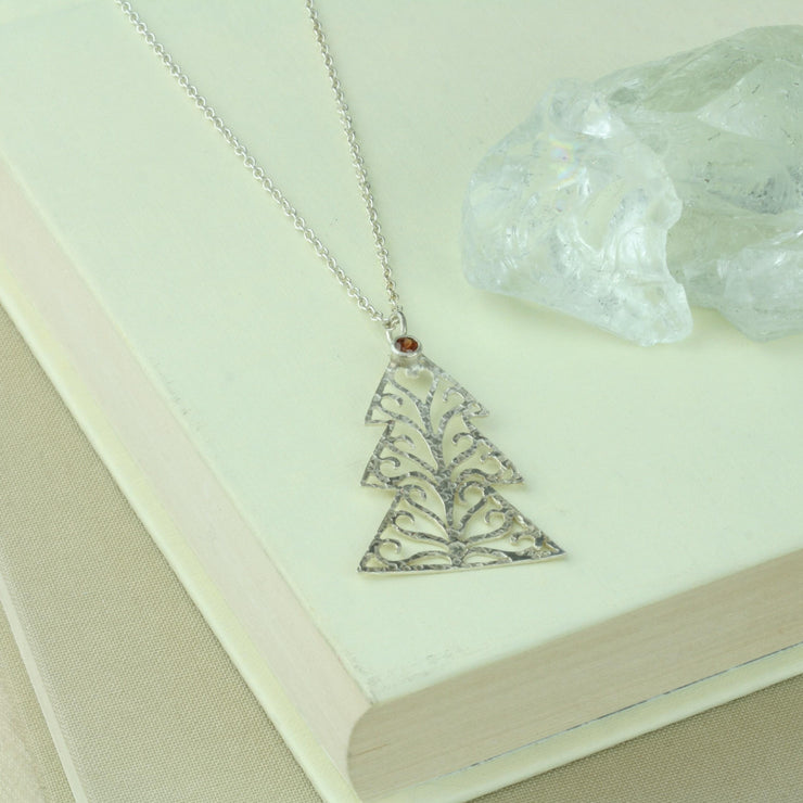 Silver pendant necklace in the shape of a Christmas three with three layers. The tree features a hand drawn pattern which is hand sawn with swirls from the centre to the sides. It has a hammered texture which has been polished to a shiny finish, giving it a shimmer effect. Seen here with a matching set of silver Christmas tree hook earrings.