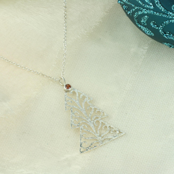 Silver pendant necklace in the shape of a Christmas three with three layers. The tree features a hand drawn pattern which is hand sawn with swirls from the centre to the sides. It has a hammered texture which has been polished to a shiny finish, giving it a shimmer effect. Seen here with a matching set of silver Christmas tree hook earrings.