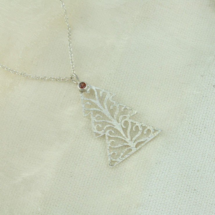 Silver pendant necklace in the shape of a Christmas three with three layers. The tree features a hand drawn pattern which is hand sawn with swirls from the centre to the sides. It has a hammered texture which has been polished to a shiny finish, giving it a shimmer effect. Seen here with a matching set of silver Christmas tree hook earrings.