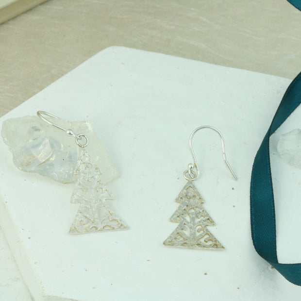 Silver hook earrings in the shape of a Christmas three with three layers. The trees feature a hand drawn pattern which is hand sawn with swirls from the centre to the sides. They have a hammered texture which has been polished to a shiny finish, giving them a shimmer effect. 